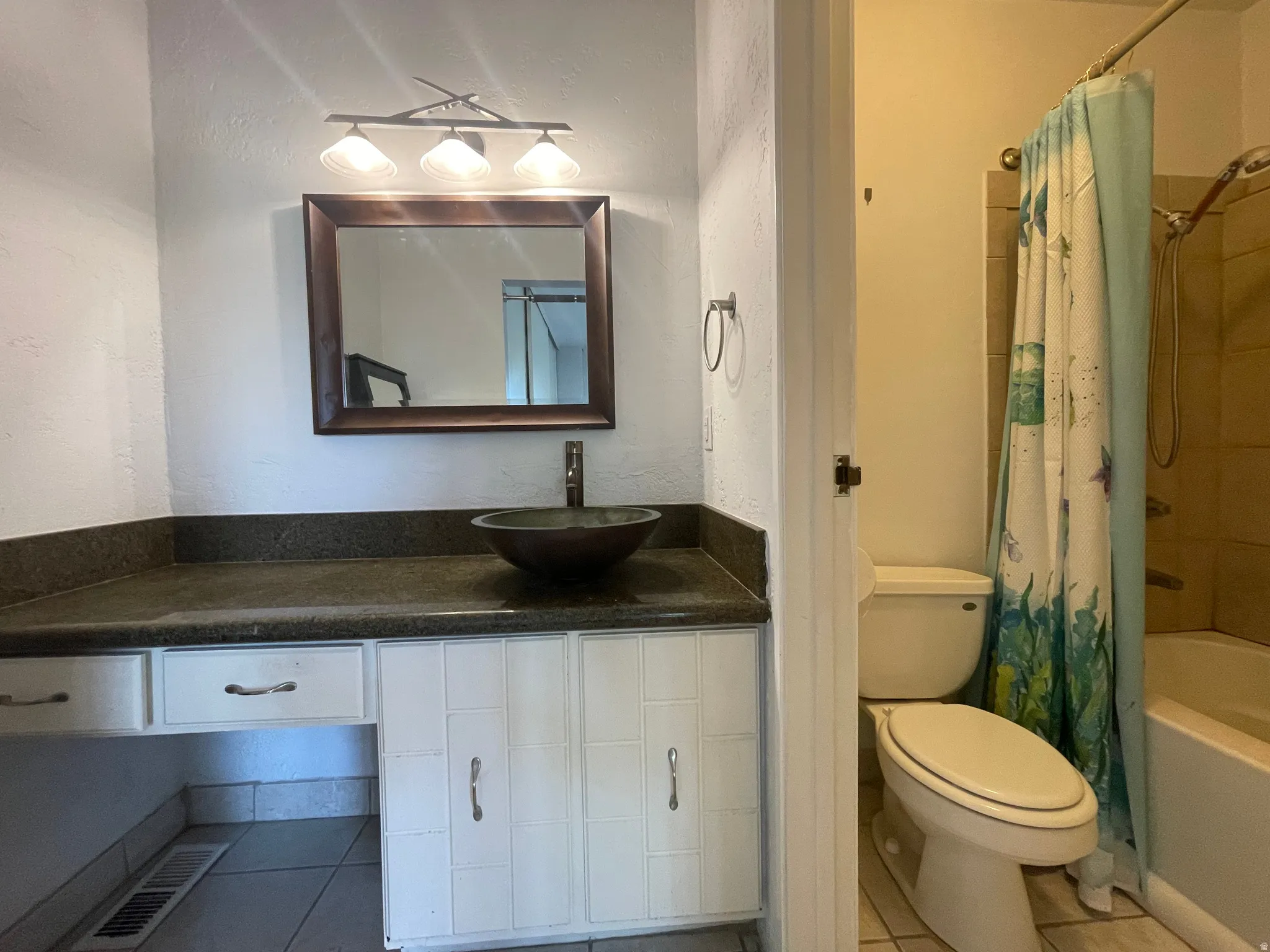 Full en-suite private bathroom featuring shower / bath combo with shower curtain, separate vanity area, tile patterned floors, and a textured wall