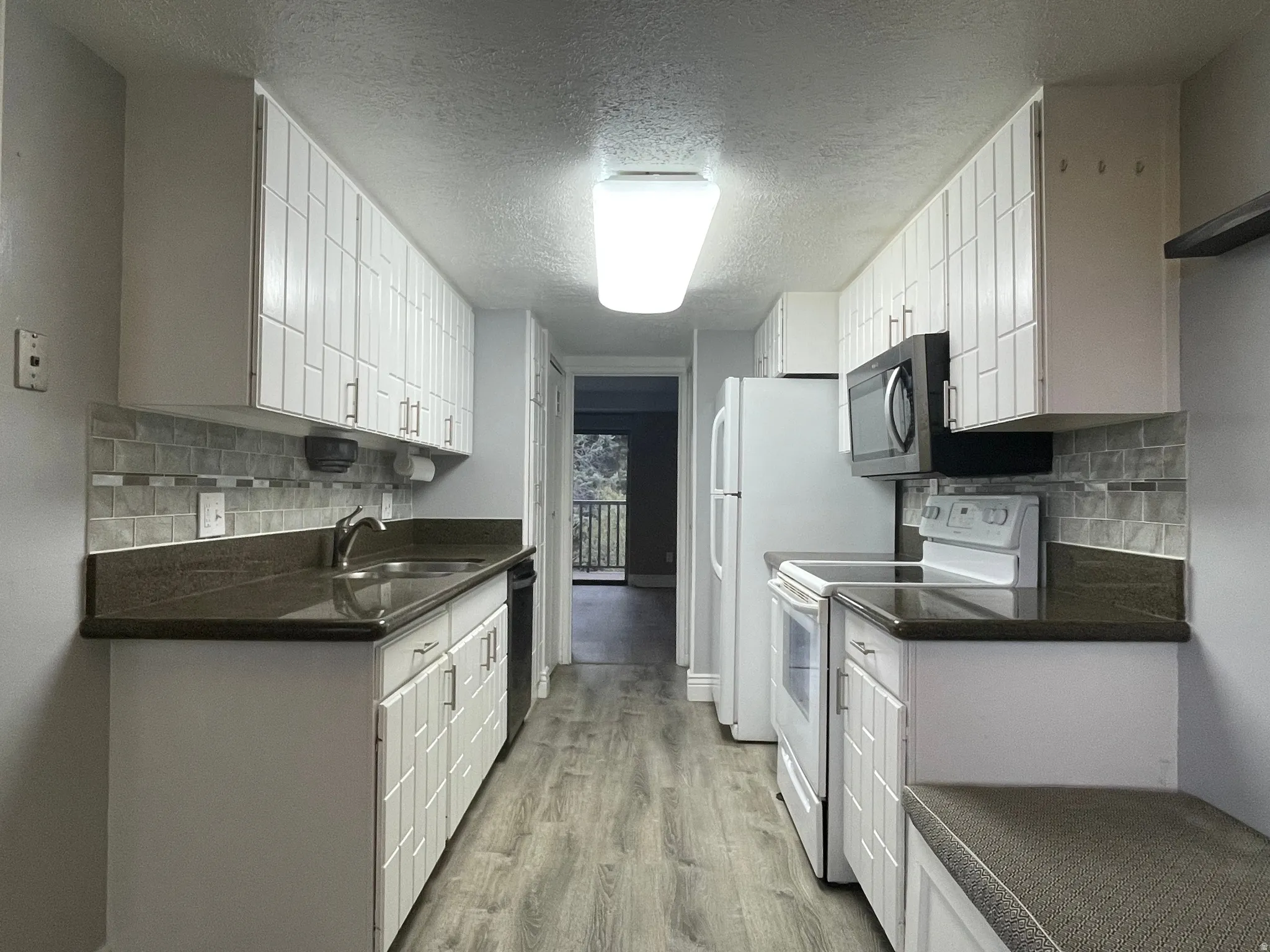 Light, bright kitchen with a textured ceiling, white cabinets, white/stainless appliances, decorative backsplash, and light wood-style floors