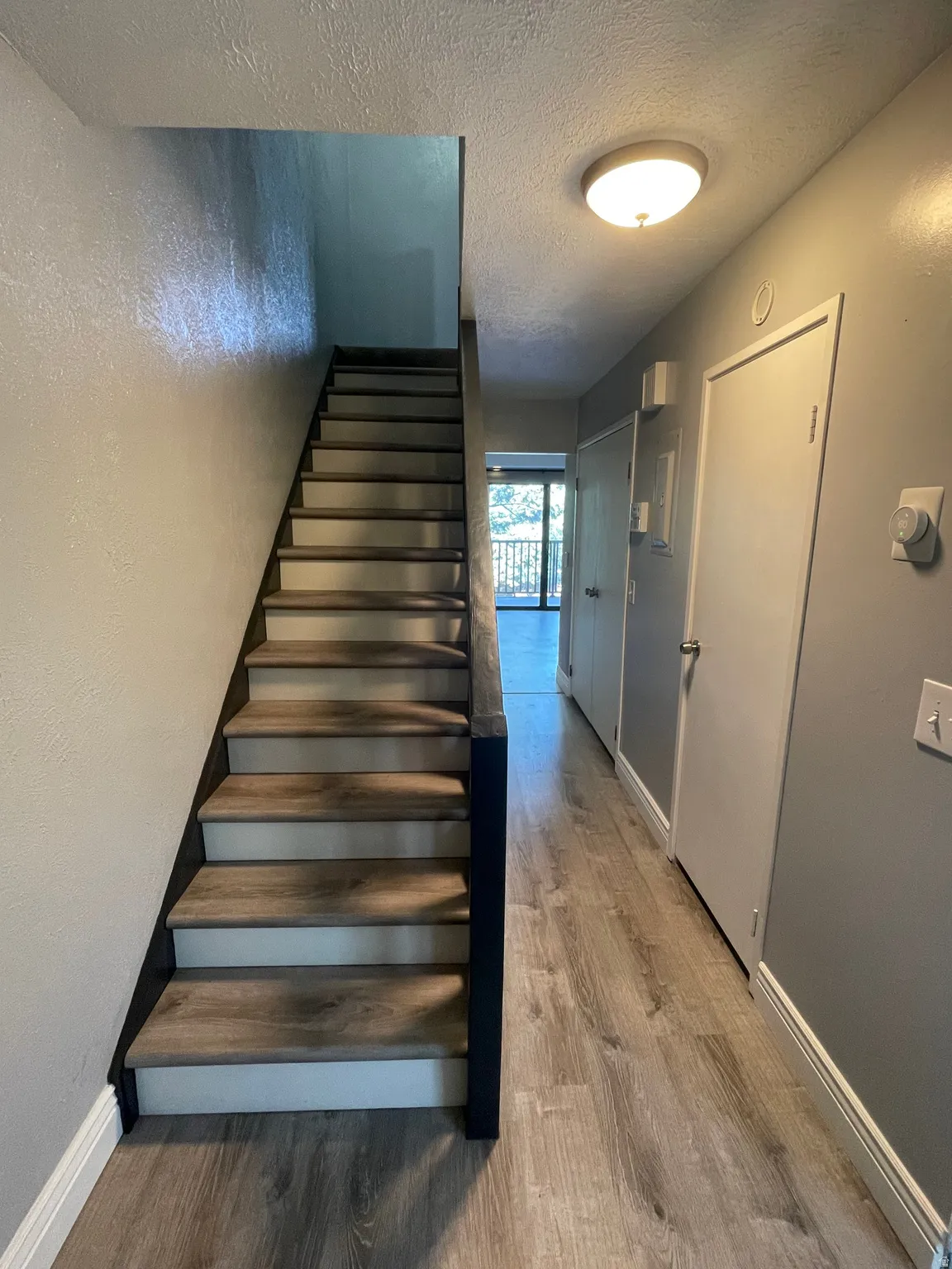 Stairs with a textured ceiling, wood finished floors, and a textured wall