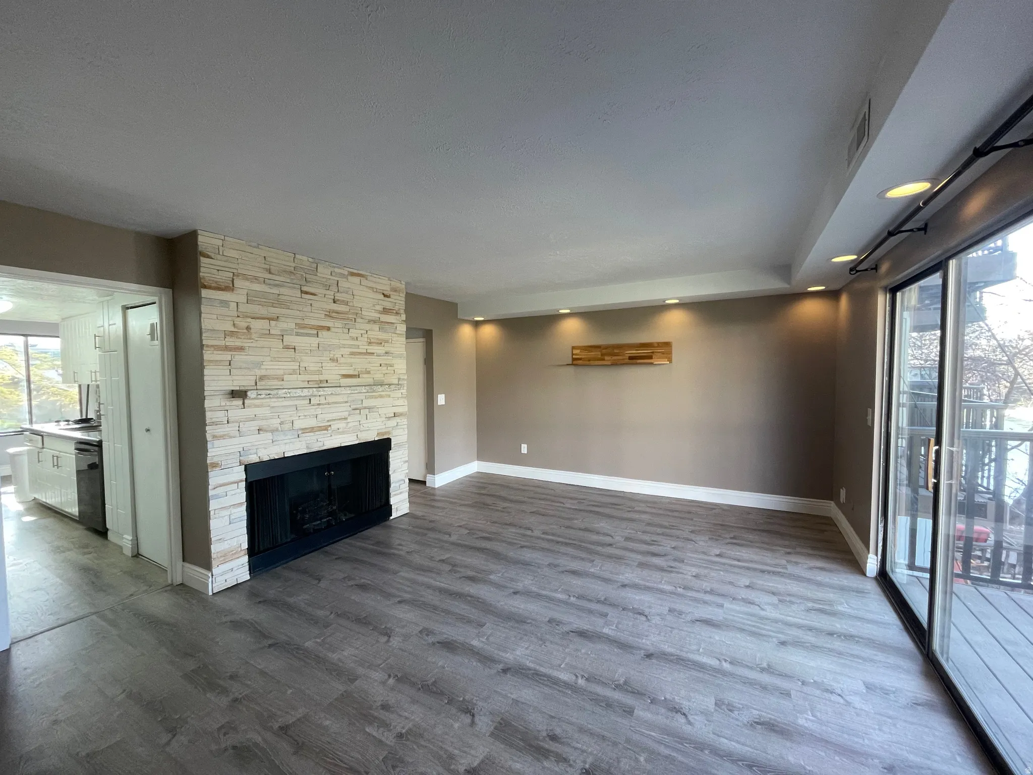 Unfurnished living room with a stone fireplace, lots of recessed lighting, and dark wood-style floors