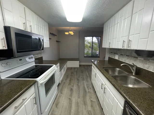 Kitchen featuring white electric stove, white cabinets, stainless steel microwave, and a textured ceiling