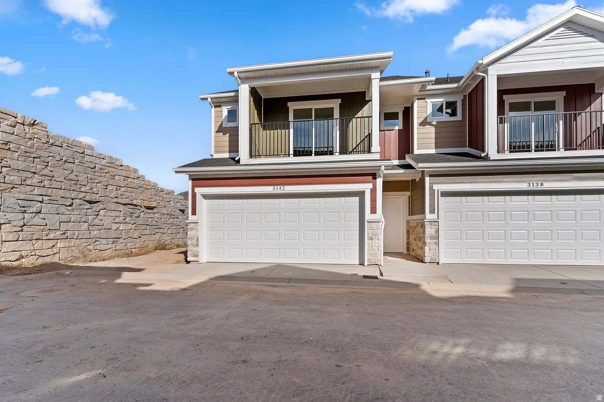 View of front of home featuring stone siding, a balcony, and an attached garage
