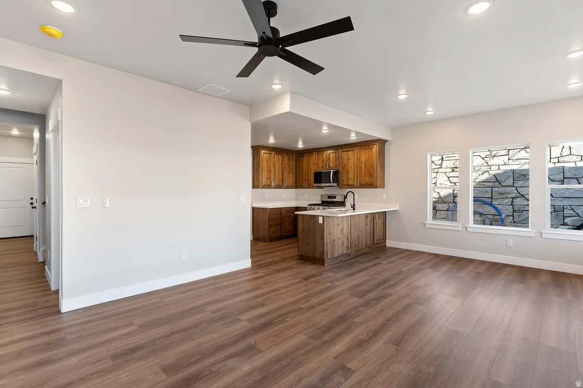 Kitchen with a peninsula, light countertops, wood finish cabinetry, a ceiling fan, and dark wood-style floors