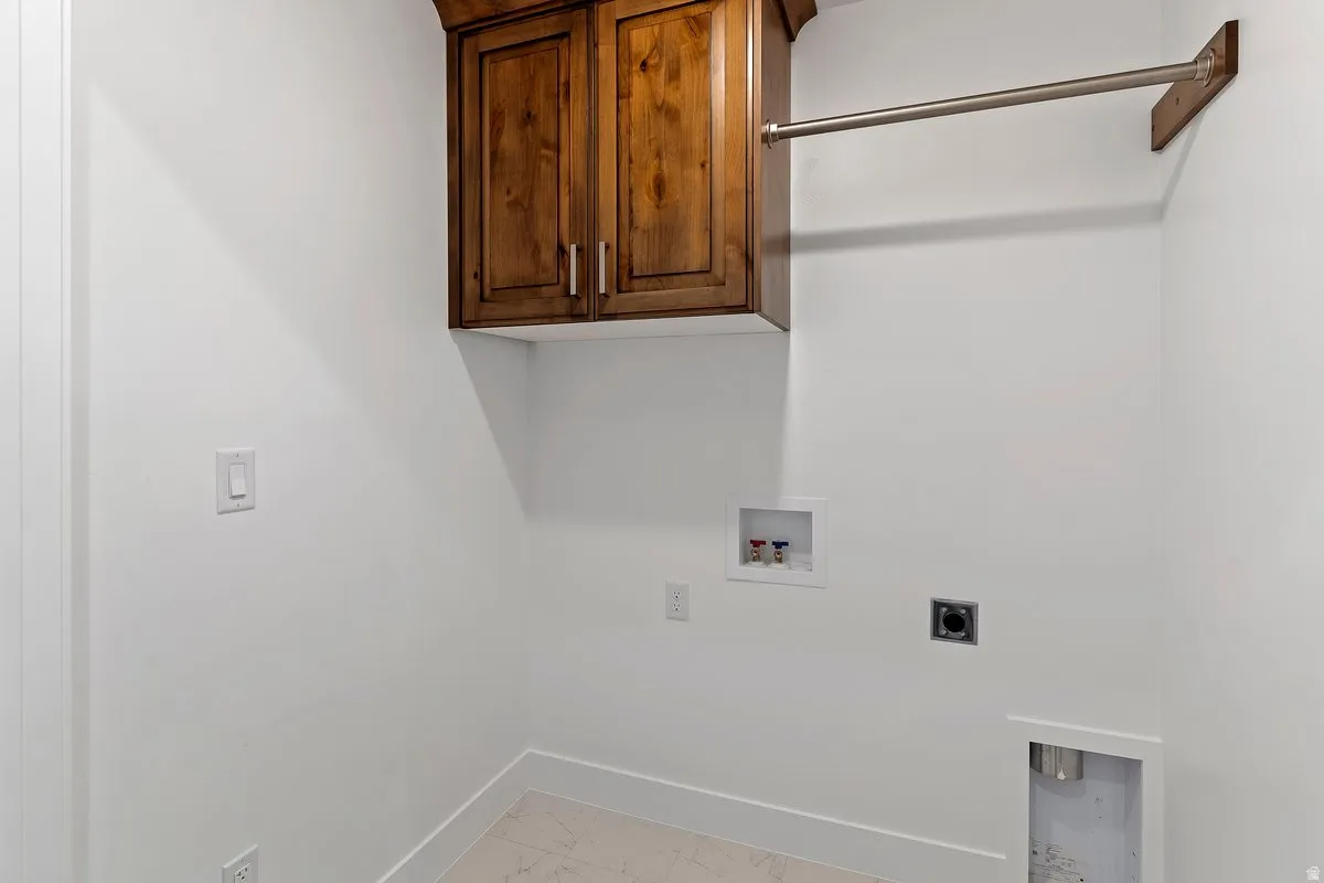 Laundry area featuring electric dryer hookup, cabinet space, washer hookup, and light marble finish flooring