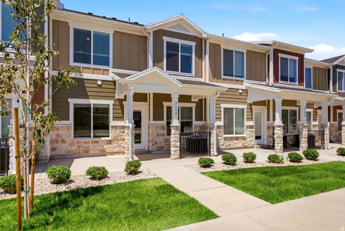 Modern townhome exterior featuring multi-toned siding, stone accents, white trim, a covered entry, and a manicured lawn