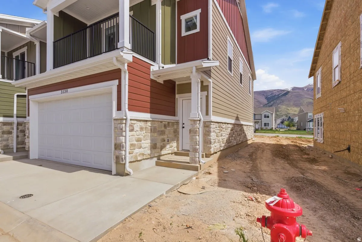 Doorway to property with stone siding, an attached garage, a mountain view, board and batten siding, and concrete driveway