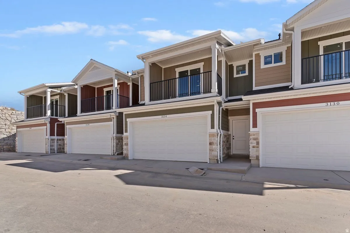 View of front of home with a balcony, stone siding, a garage, and board and batten siding