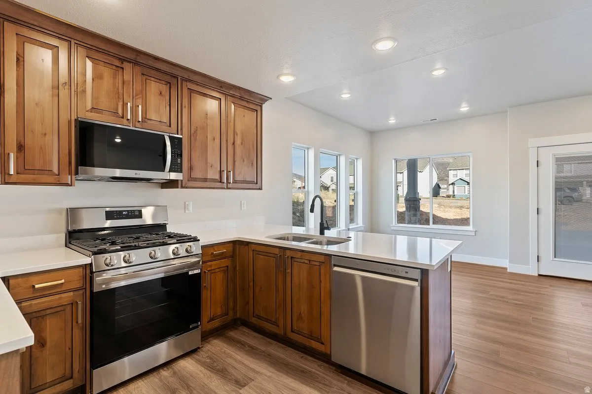 Kitchen featuring stainless steel appliances, dark wood-style flooring, a peninsula, light stone countertops, and wood finish cabinetry