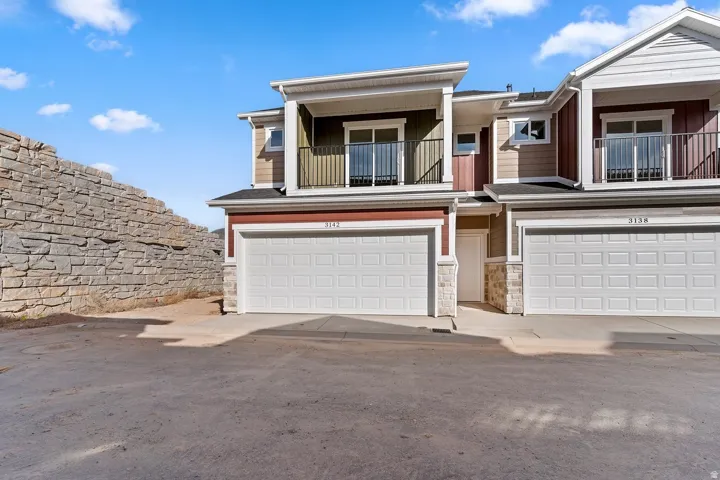 View of front of home featuring stone siding, a balcony, and an attached garage