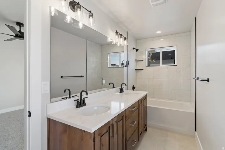 Full bathroom with double vanity, a ceiling fan, and washtub / shower combination