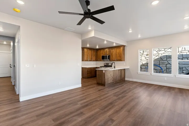 Kitchen with a peninsula, light countertops, wood finish cabinetry, a ceiling fan, and dark wood-style floors