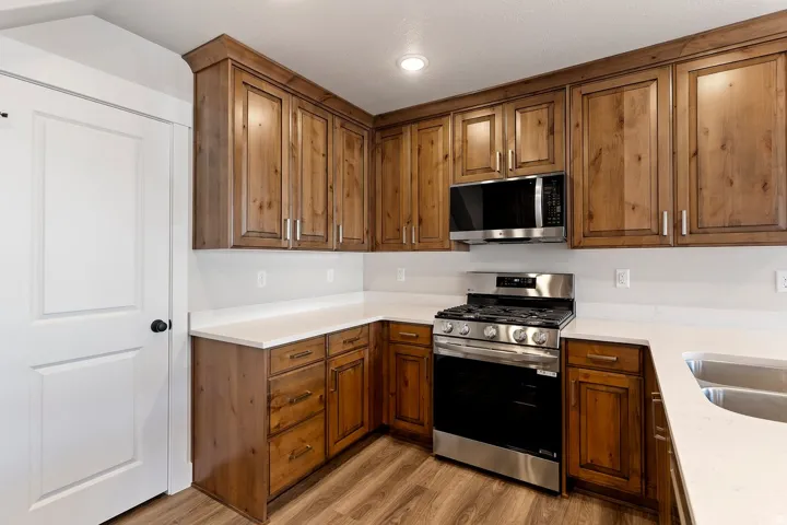 Kitchen featuring stainless steel appliances, wood finish cabinetry, light wood-style flooring, and light stone countertops