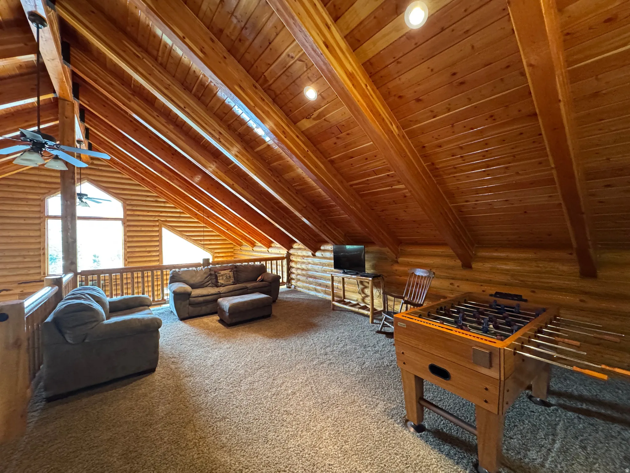 Loft  featuring log walls, carpet floors, a ceiling fan, and a wooden ceiling with exposed beams
