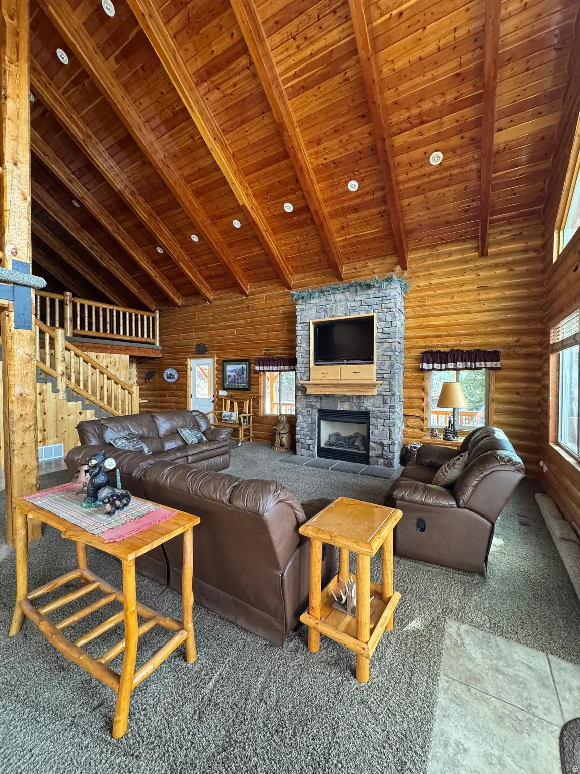 Great Room featuring carpet floors, a high wood beamed ceiling, log walls, and a stone fireplace