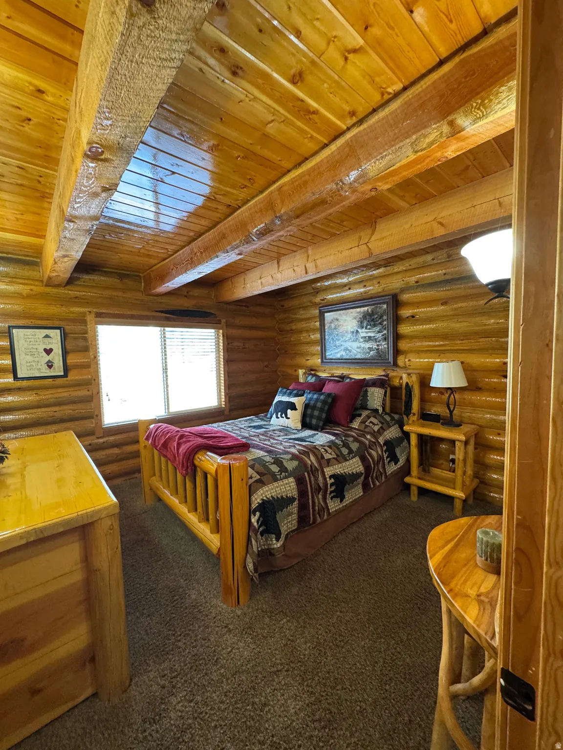 Bedroom with a wood ceiling with exposed beams, log walls, and dark colored carpet