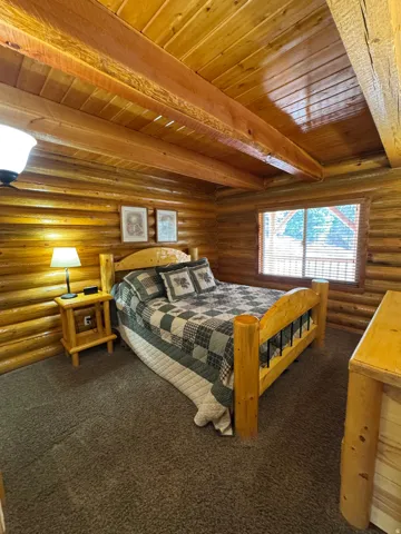 Bedroom with a wood ceiling with exposed beams, rustic walls, and carpet flooring