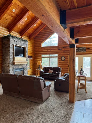 Carpeted living area with a high wood beamed ceiling, a stone fireplace, tile patterned flooring, log walls, and french doors