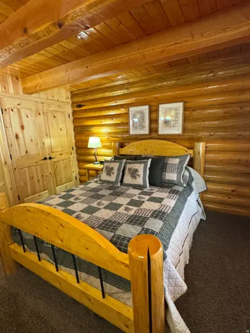 Bedroom featuring carpet, rustic walls, and a wood ceiling with exposed beams