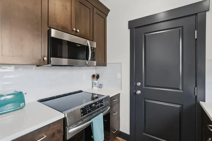 Kitchen featuring stainless steel appliances, dark wood finish cabinetry, backsplash, and light stone counters