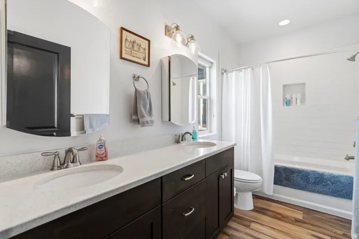 Full bath featuring double vanity, light wood-type flooring, and shower / tub combo