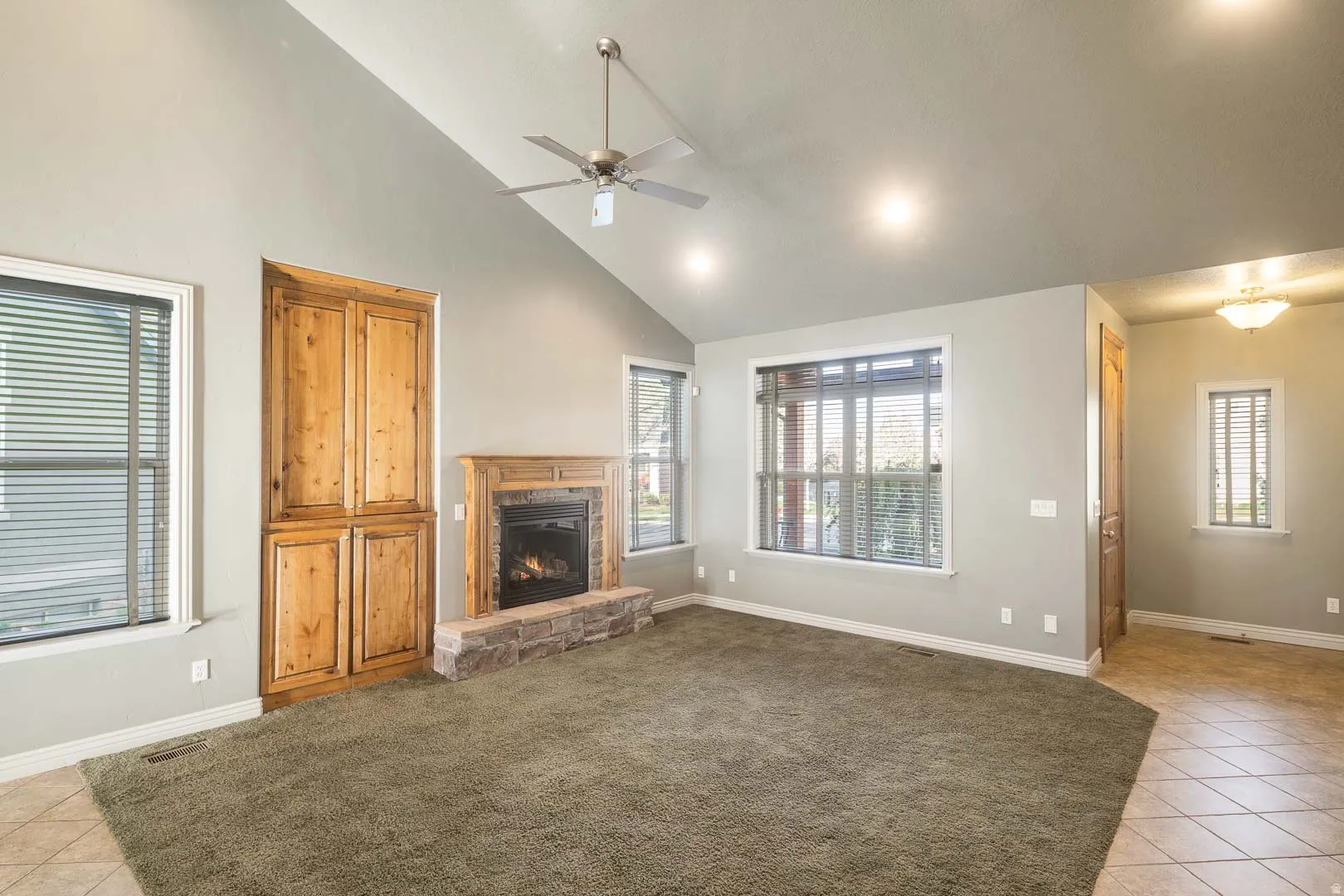Unfurnished living room featuring light tile patterned floors, a ceiling fan, lofted ceiling, a stone fireplace, and healthy amount of natural light