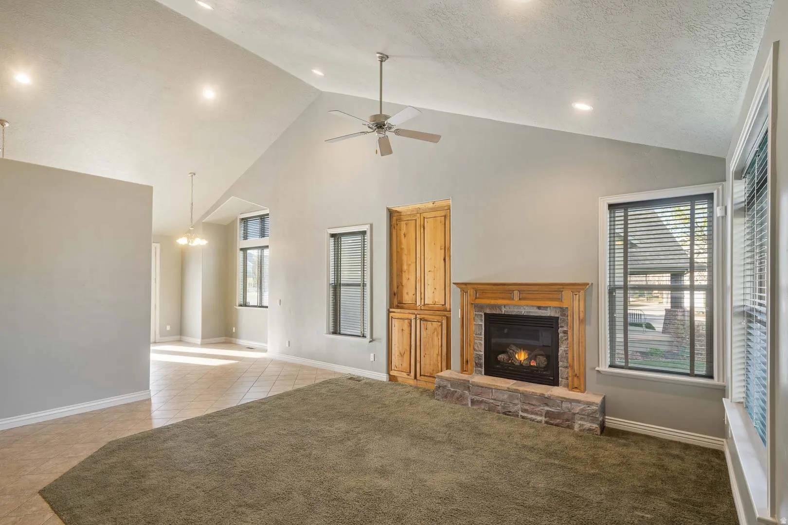 Unfurnished living room with a stone fireplace, ceiling fan, light carpet, recessed lighting, and light tile patterned flooring
