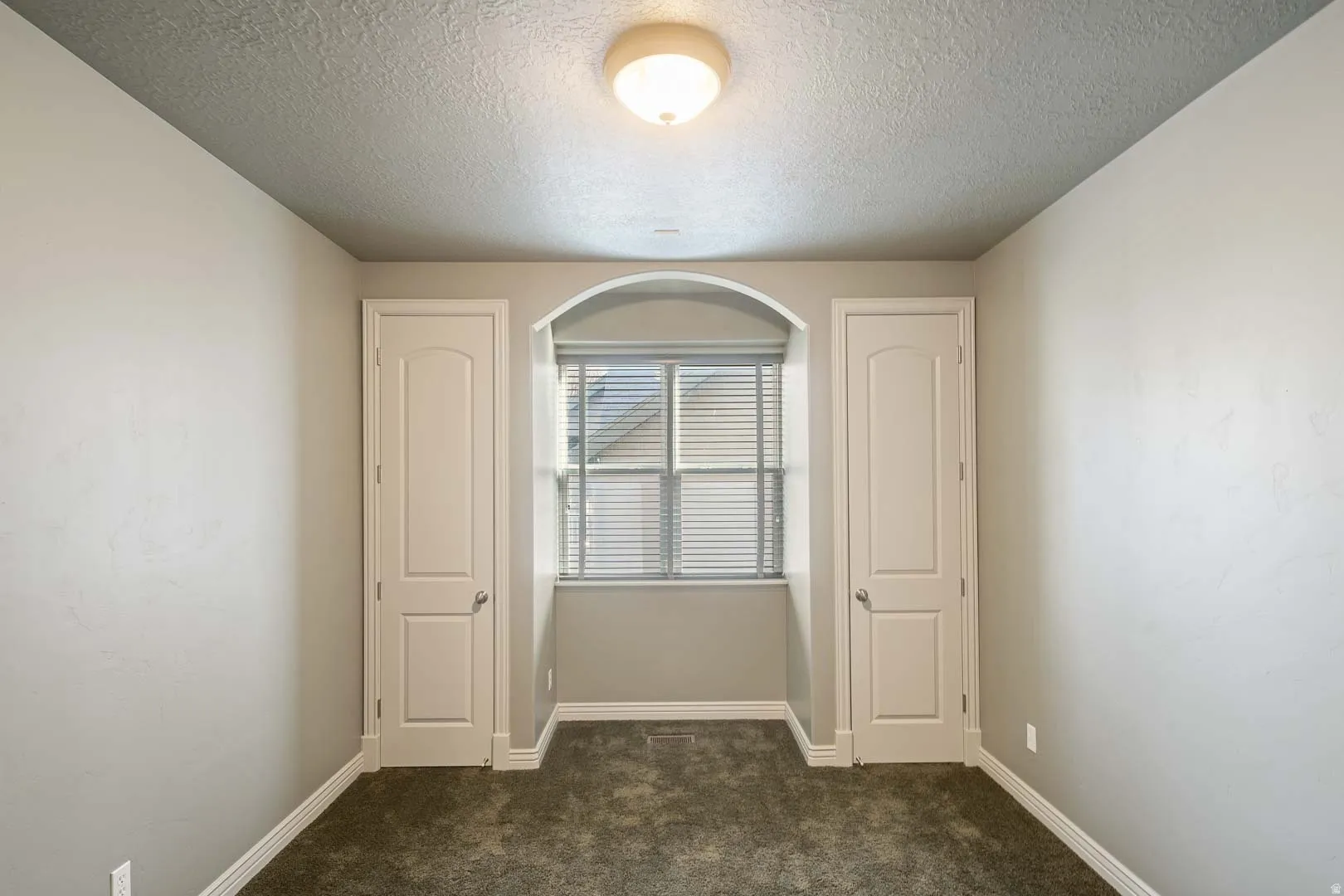Unfurnished room with dark colored carpet and a textured ceiling