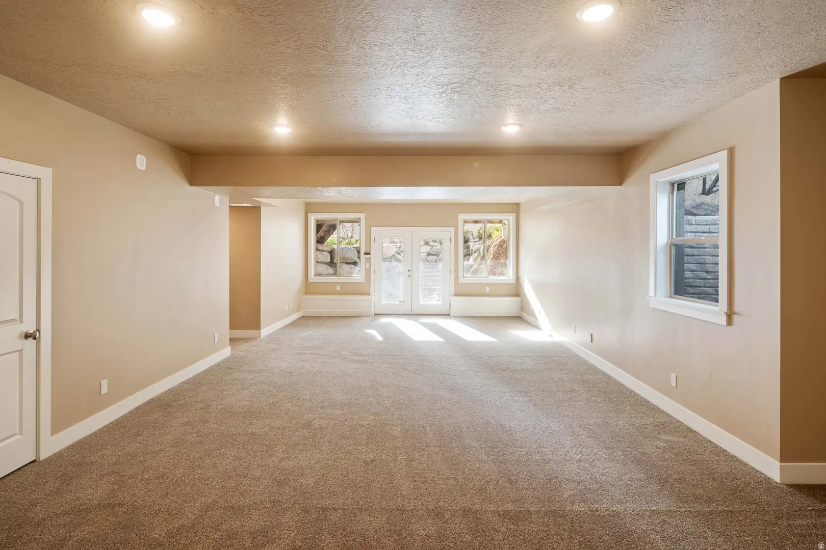 Spare room with french doors, a textured ceiling, plenty of natural light, light carpet, and recessed lighting