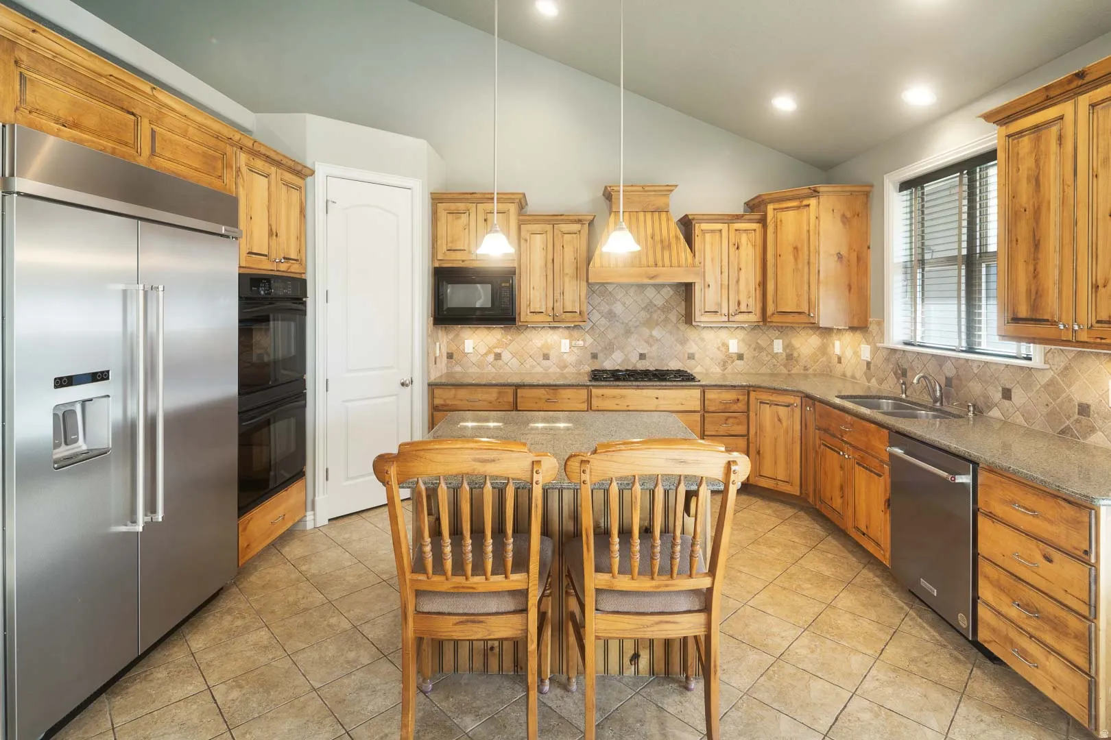Kitchen with black appliances, vaulted ceiling, dark stone countertops, hanging light fixtures, and light tile patterned floors