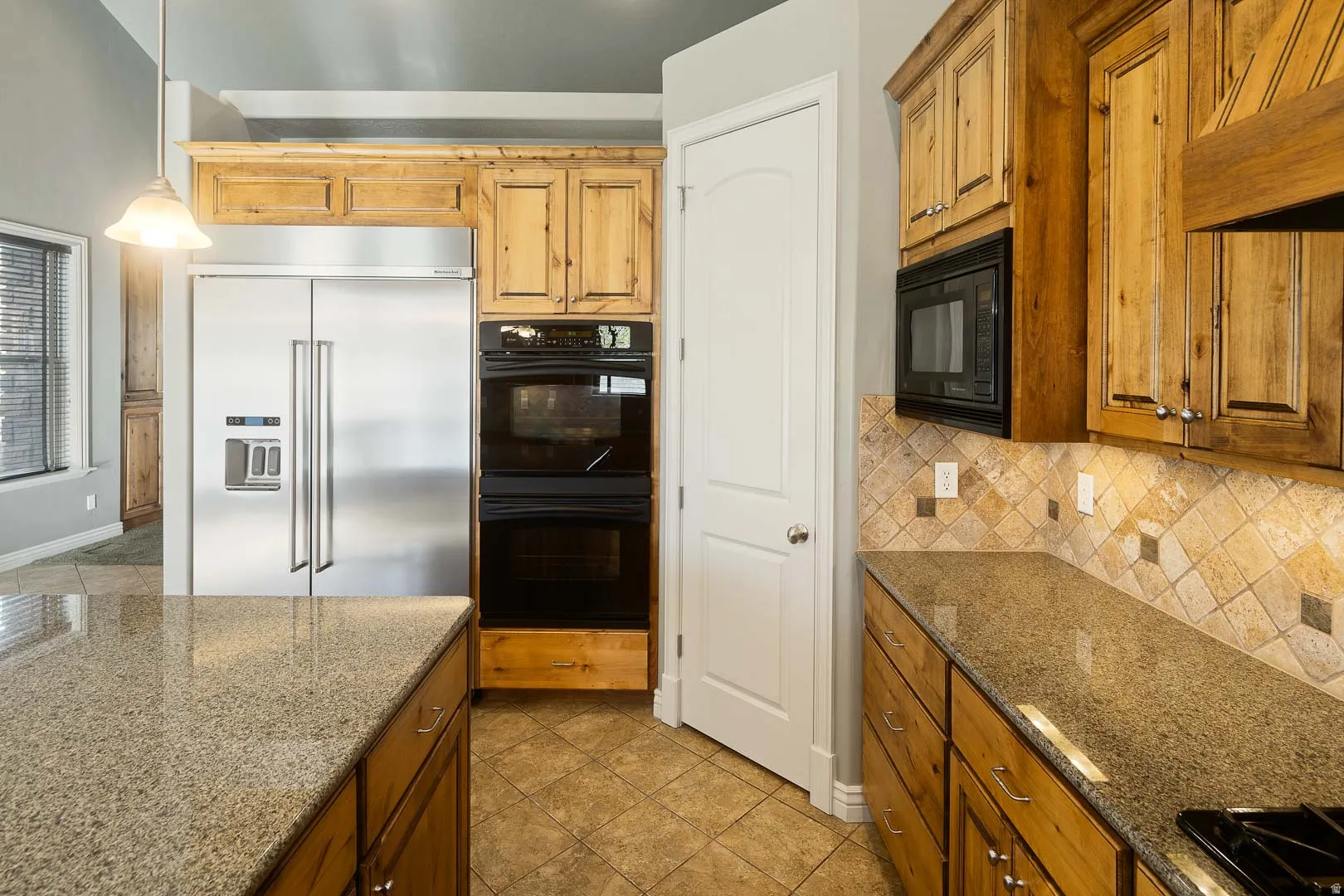 Kitchen with black appliances, dark stone counters, wood finish cabinets, and tasteful backsplash