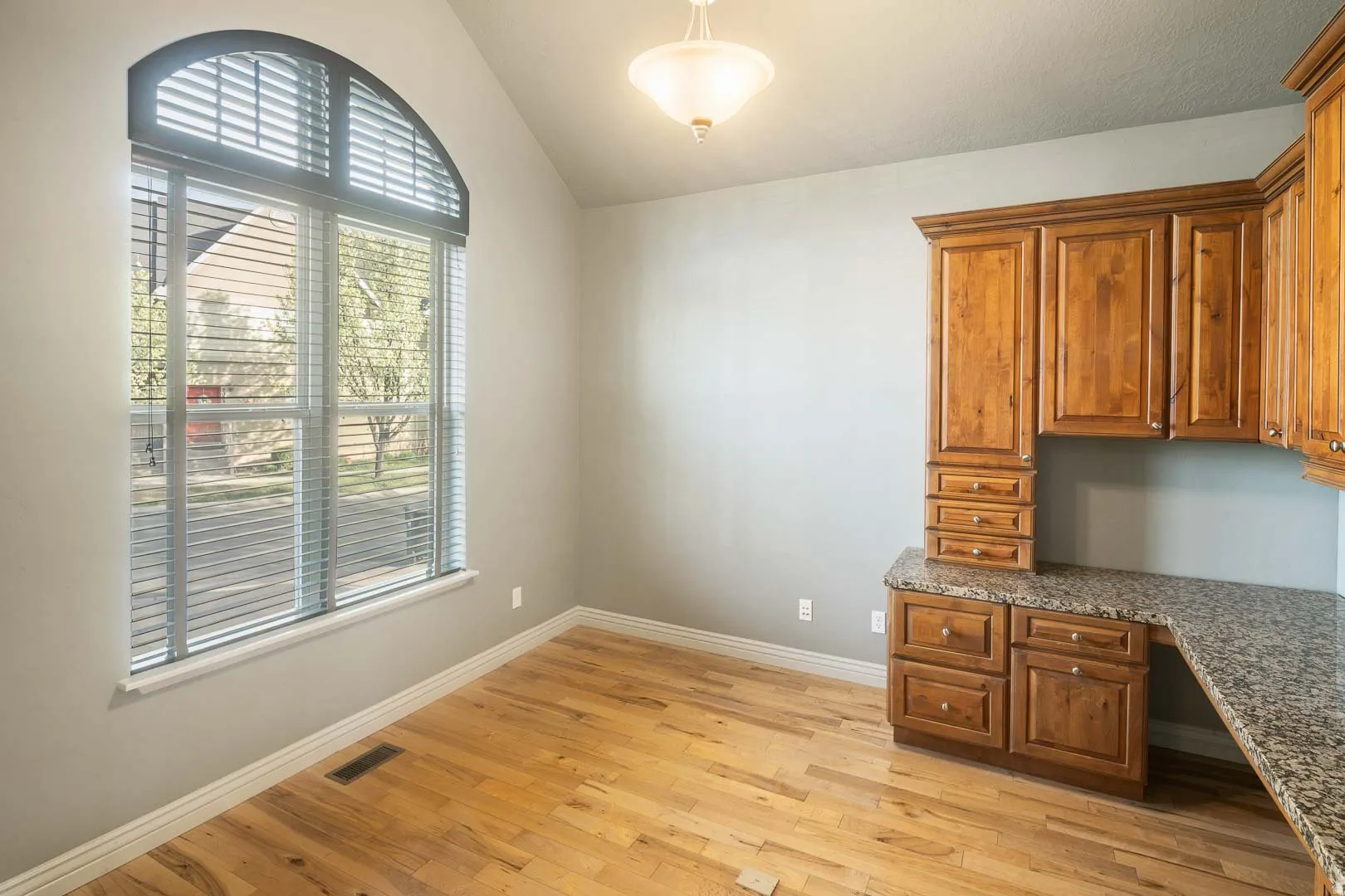 Unfurnished office with built in desk, light wood-type flooring, and lofted ceiling