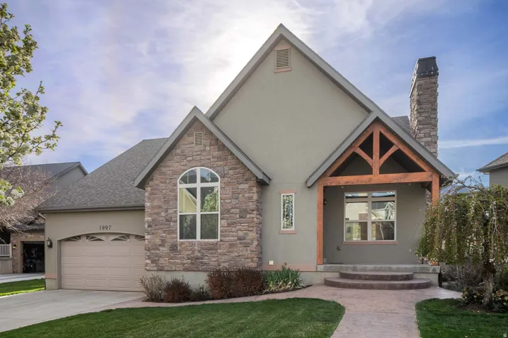 View of front of property with stucco siding, a chimney, stone siding, a garage, and concrete driveway