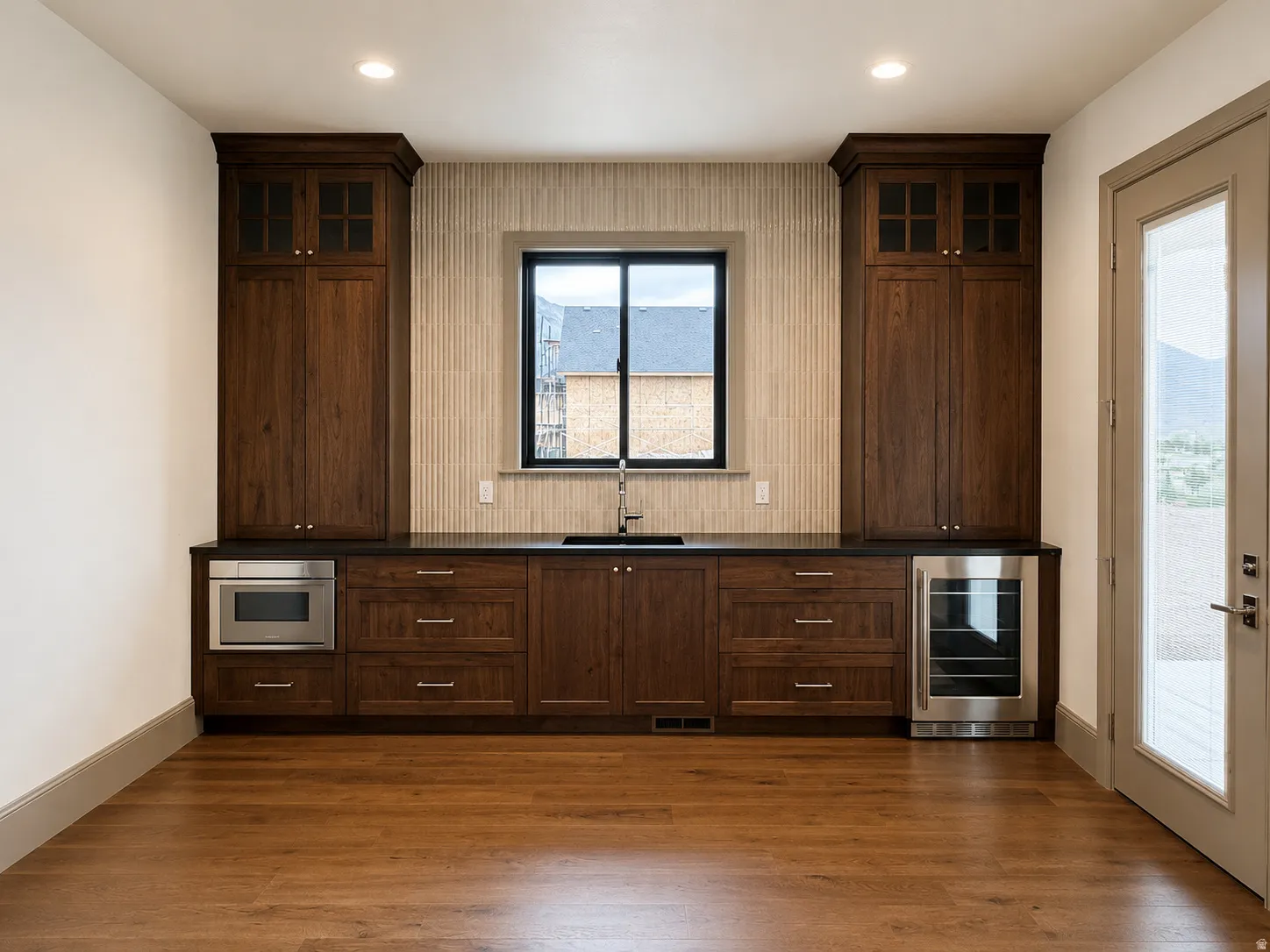 Built-in cabinetry with glass-front uppers, dark countertop, undermount sink, and wood-finish flooring