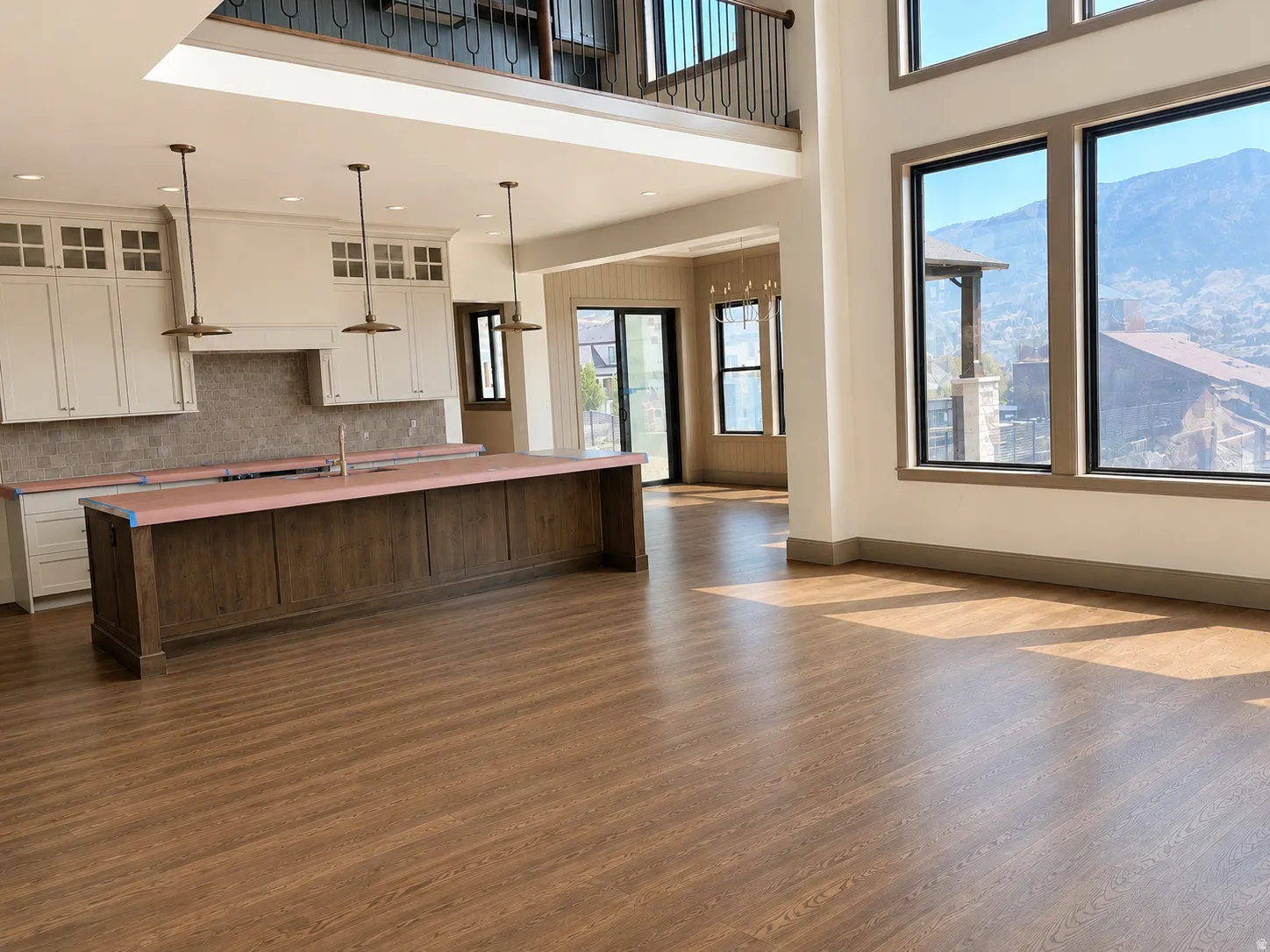 Open-concept living area with wood-finish flooring, a kitchen island, white cabinetry, a tiled backsplash, and an upper-level balcony with metal railings