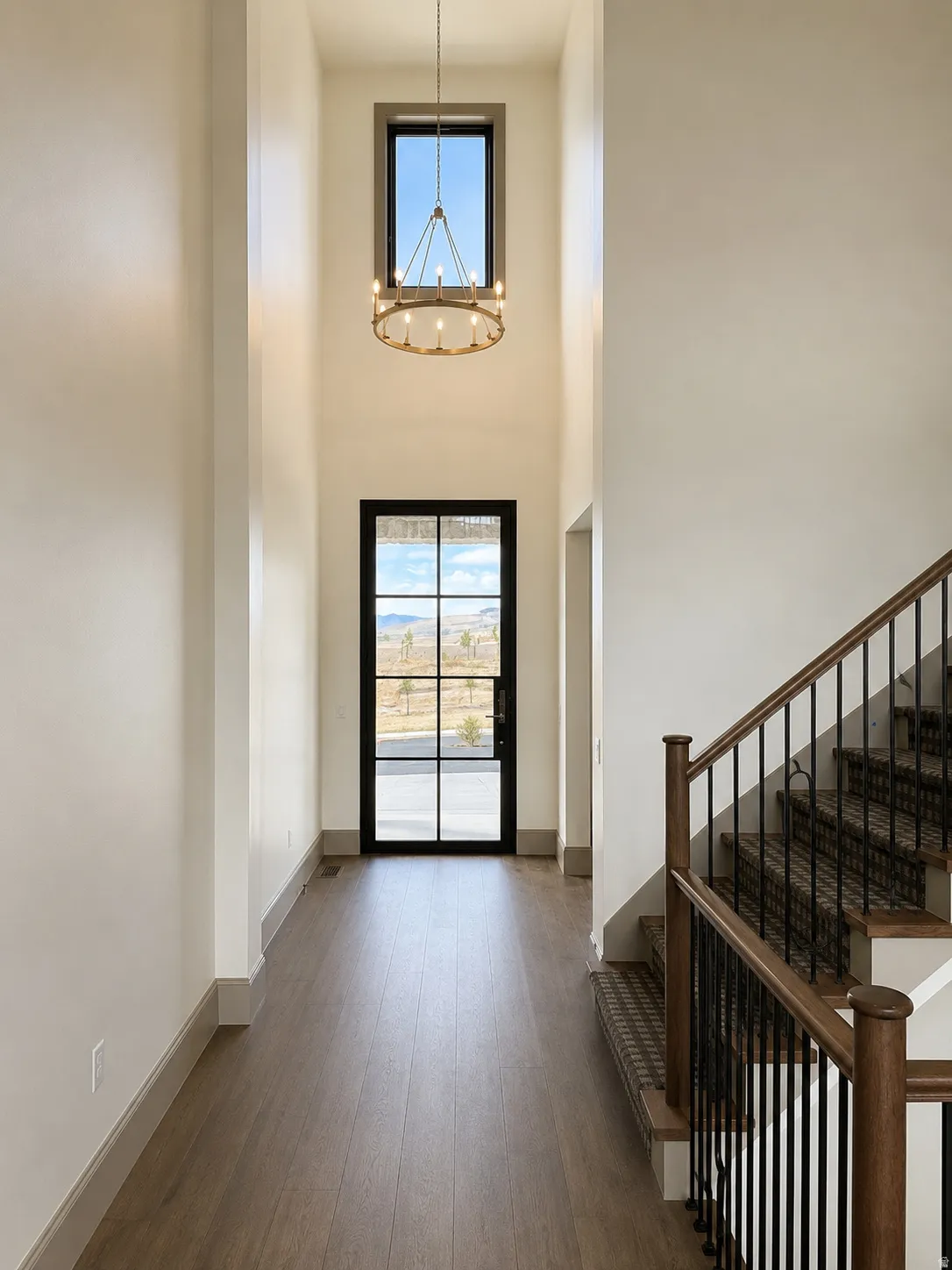 Two-story entryway with wood-finish flooring, a contemporary chandelier, and a multi-pane glass entry door