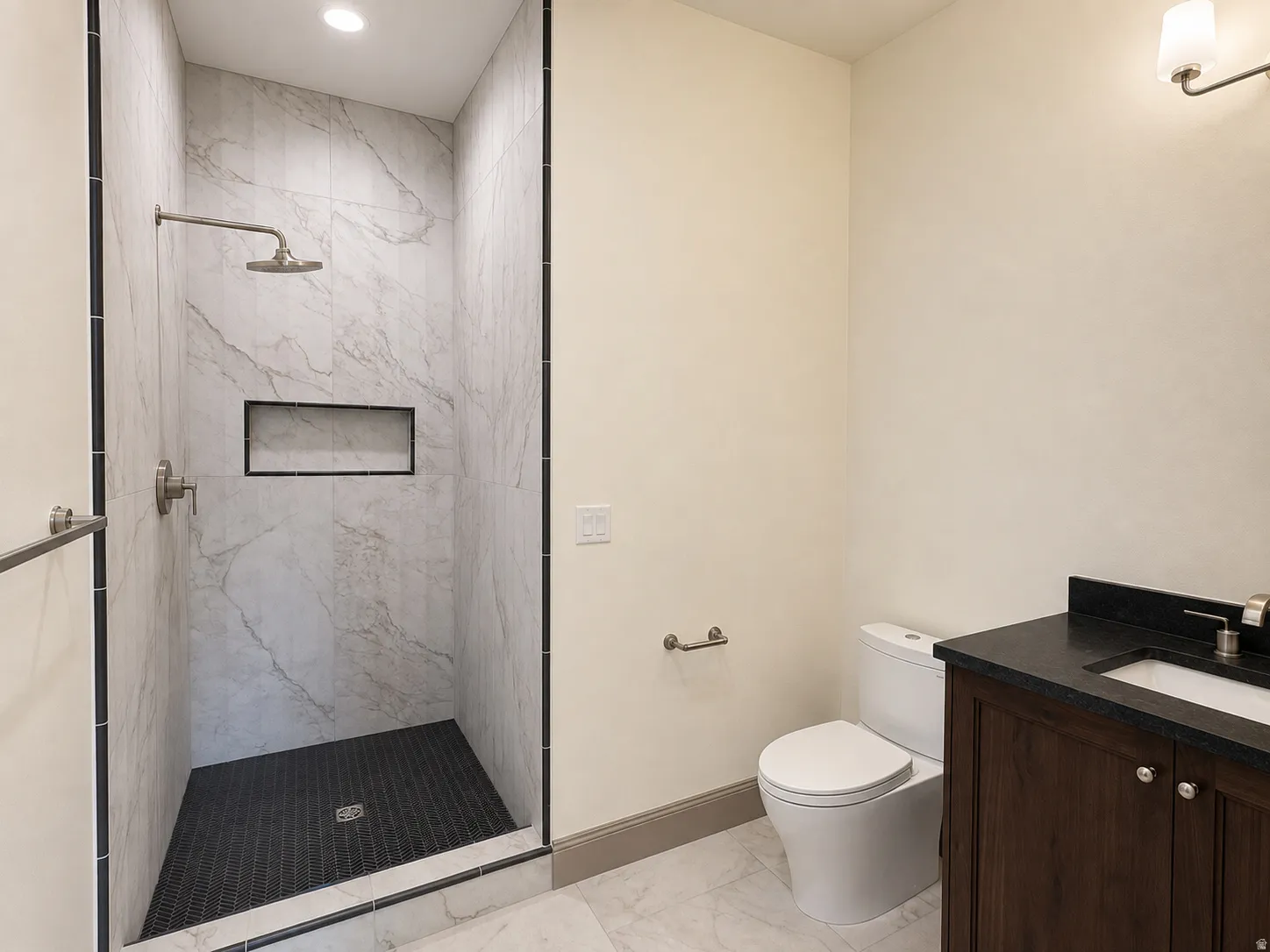 Walk-in shower with large format wall tiles, dark mosaic floor tiles, and a built-in shower niche