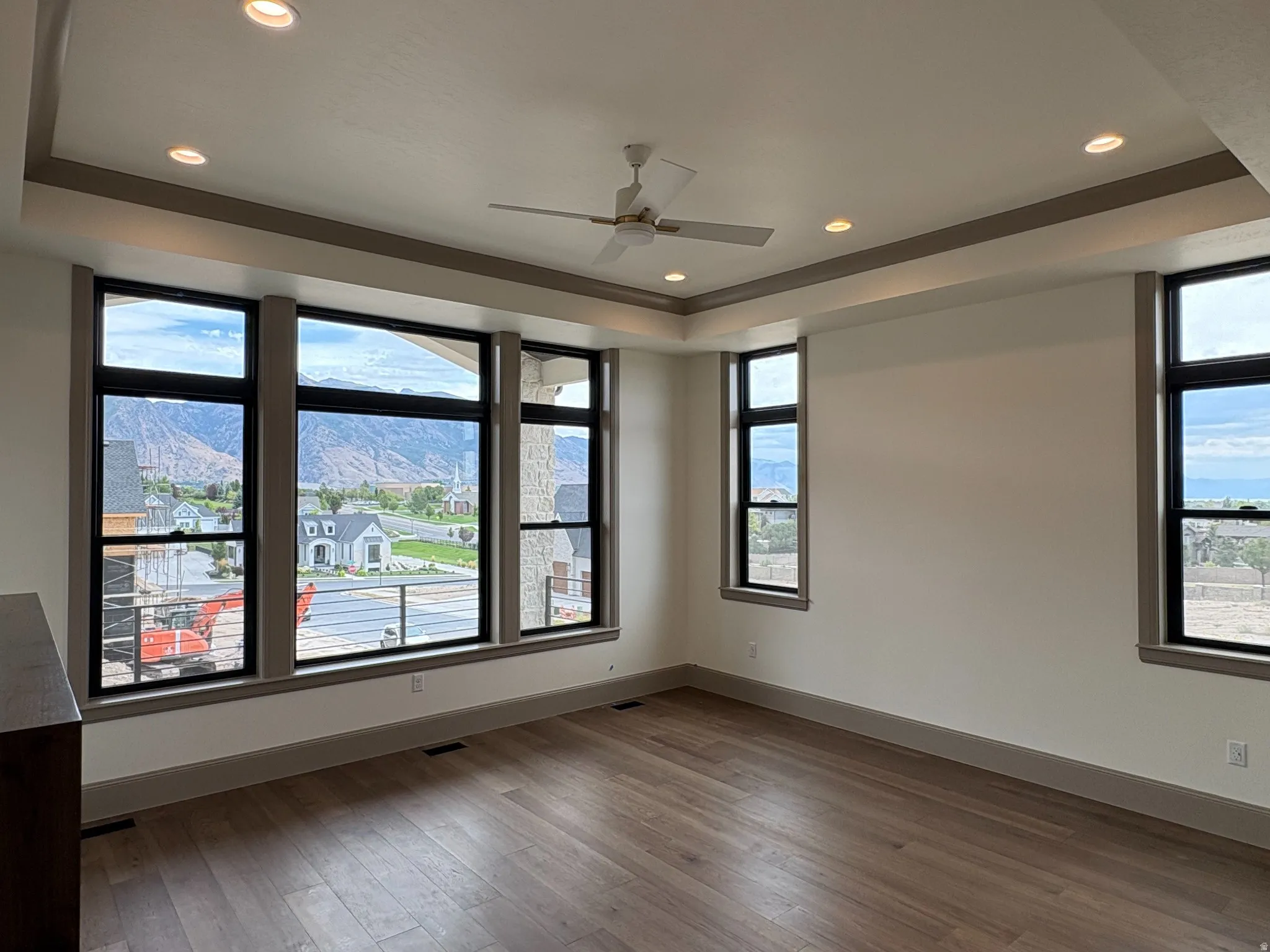 Expansive windows, tray ceiling with recessed lighting, ceiling fan, wood-finish flooring, and neutral wall tones