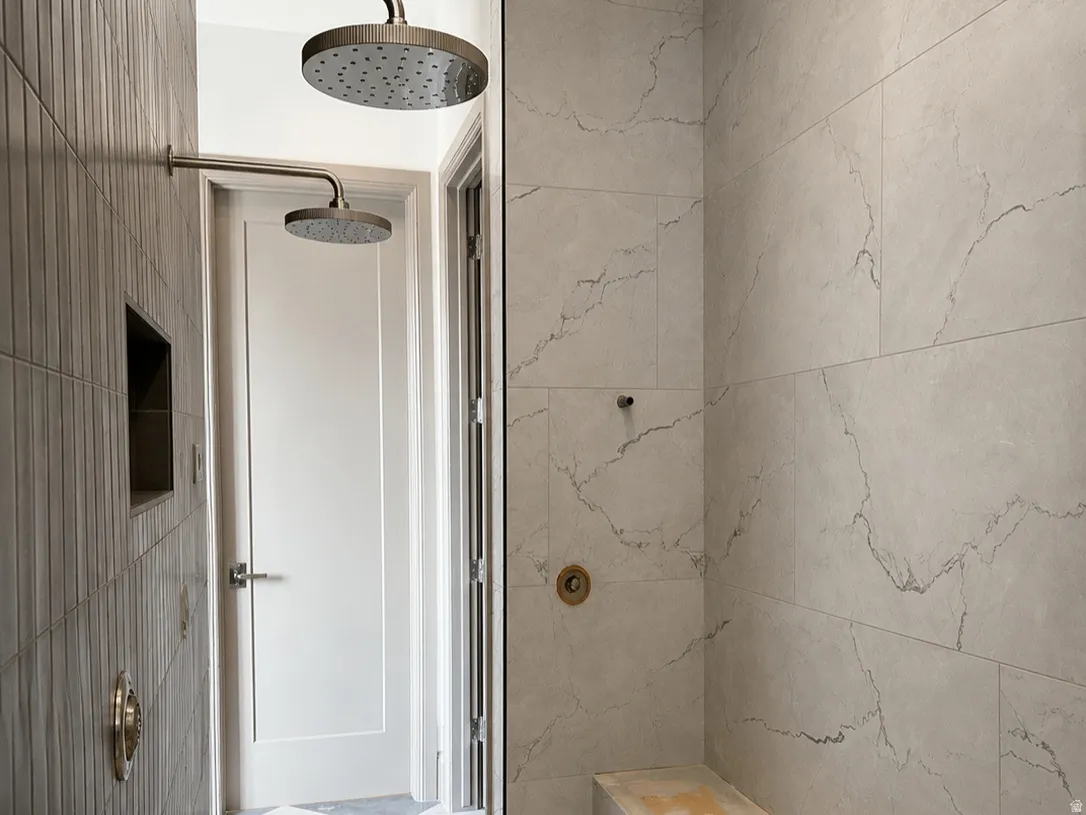 Spacious primary shower featuring dual rain shower heads, a built-in tiled bench, mosaic tile flooring, and large format wall tiling with subtle veining