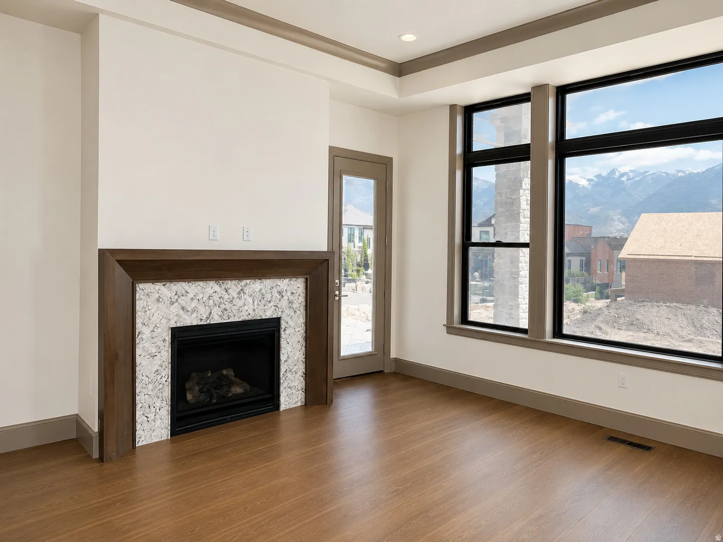 Primary bedroom featuring a fireplace with a white stone surround and dark wood mantel, large black-framed windows, wood-finish flooring, and a glass-paneled door