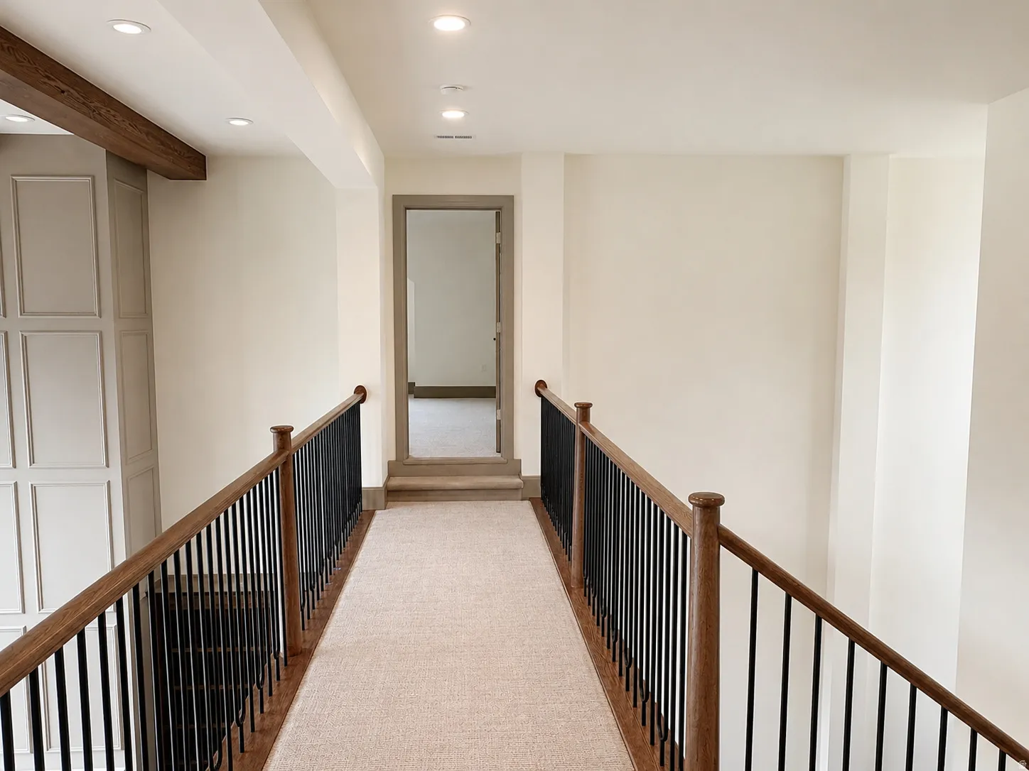Upper landing featuring a wood-finish handrail with black spindles, recessed lighting, and a neutral carpet runner