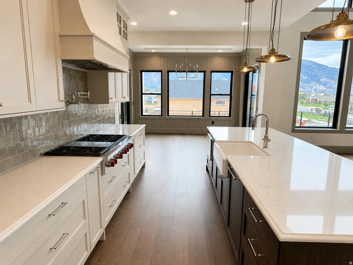 Gourmet kitchen featuring a large central island with a farmhouse sink, stainless steel range, light-toned cabinetry, and wood-finish flooring