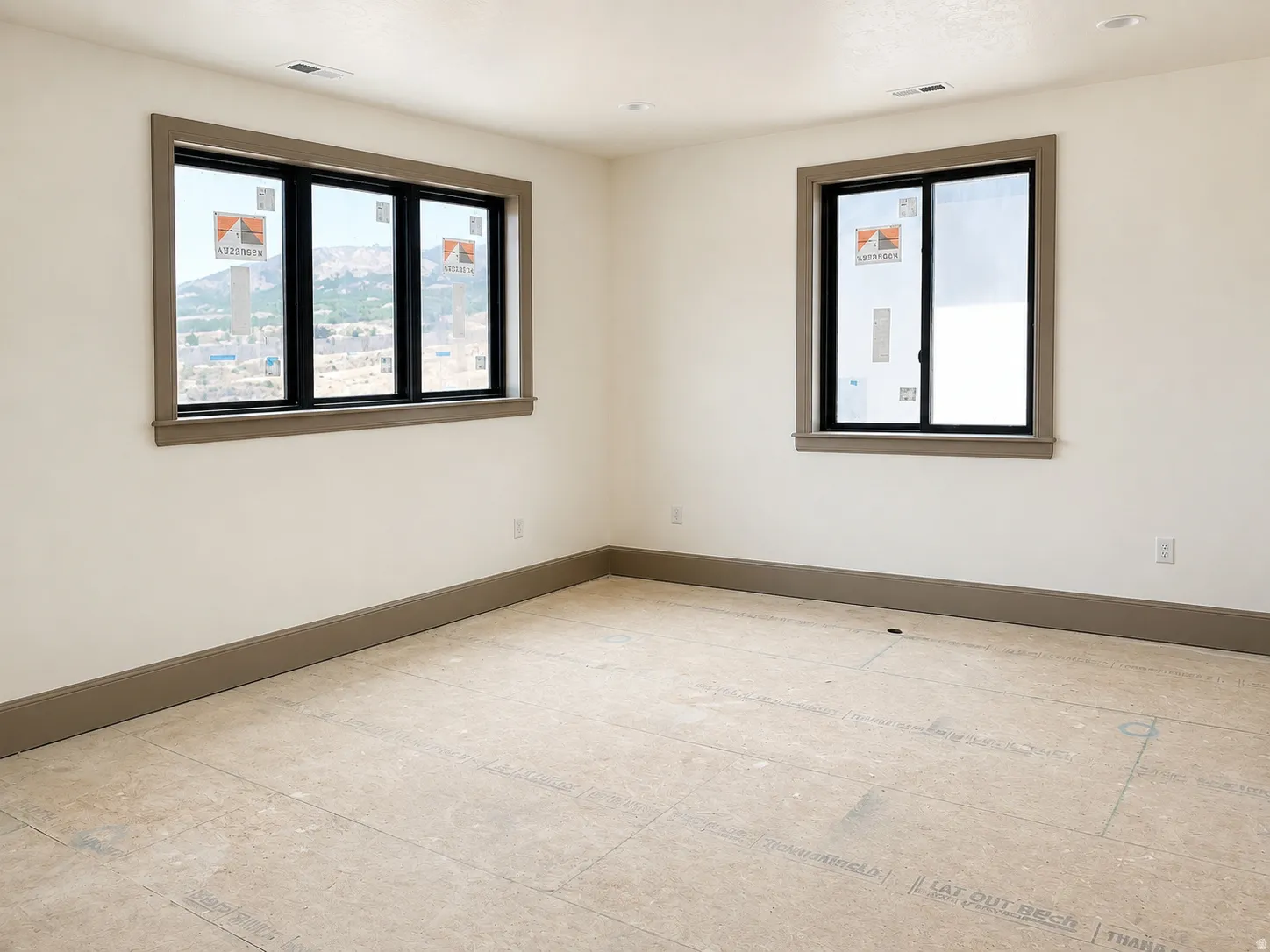 Room featuring two windows with dark trim, light walls, and a neutral-toned baseboard