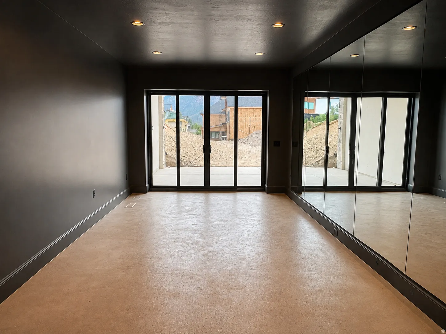 Recessed lighting illuminates an expansive room featuring a full-length mirrored wall and light-toned flooring