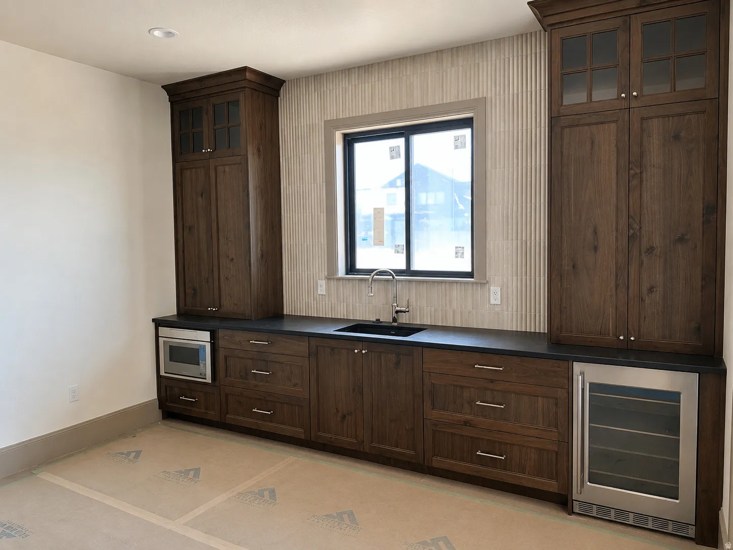 Built-in wet bar featuring dark wood-finish cabinetry, a black sink with a gooseneck faucet, a paneled tile backsplash, and dark countertops