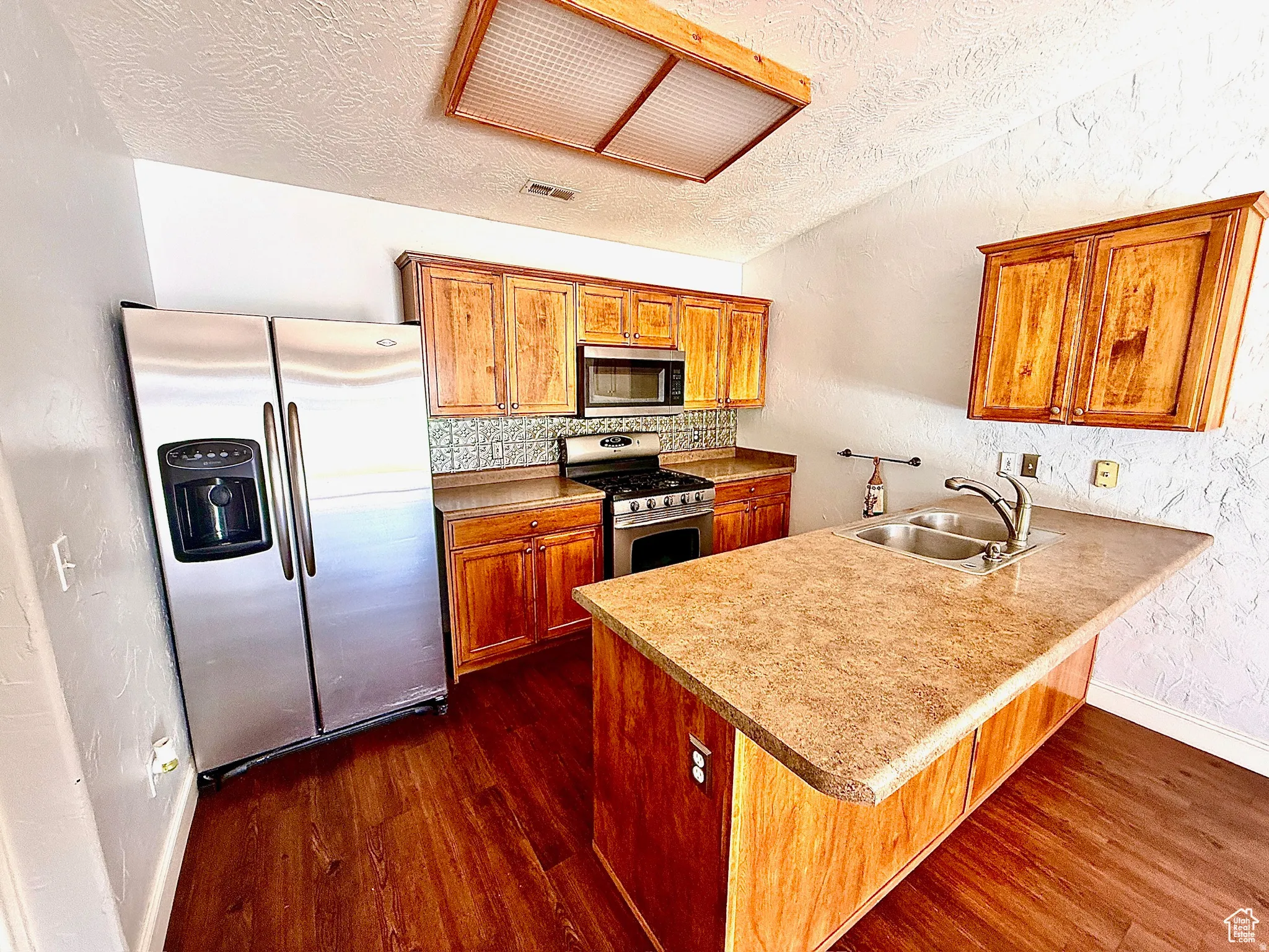 Kitchen with wood finish cabinetry, a peninsula, stainless steel appliances, dark wood-style floors, and a kitchen bar