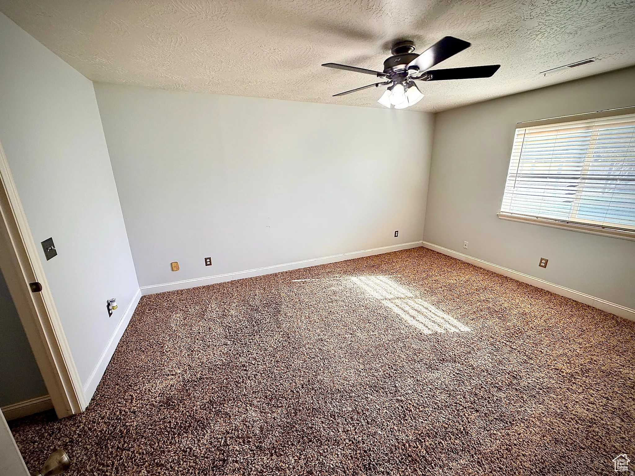 Unfurnished room with a textured ceiling, ceiling fan, and dark colored carpet