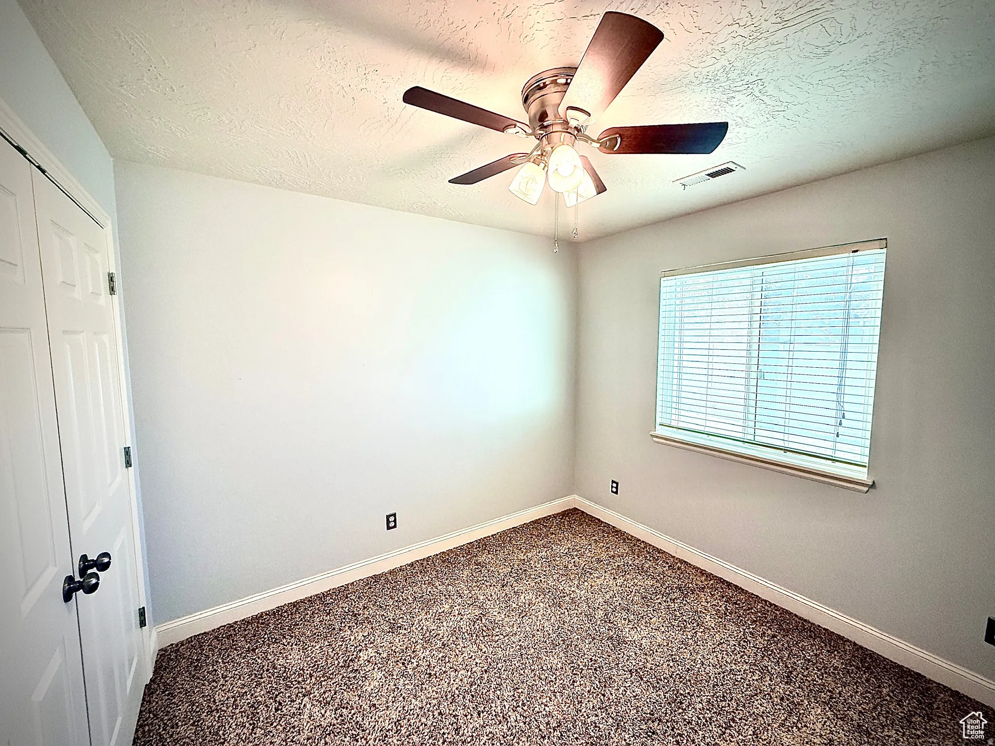 Spare room featuring a textured ceiling, ceiling fan, and dark carpet