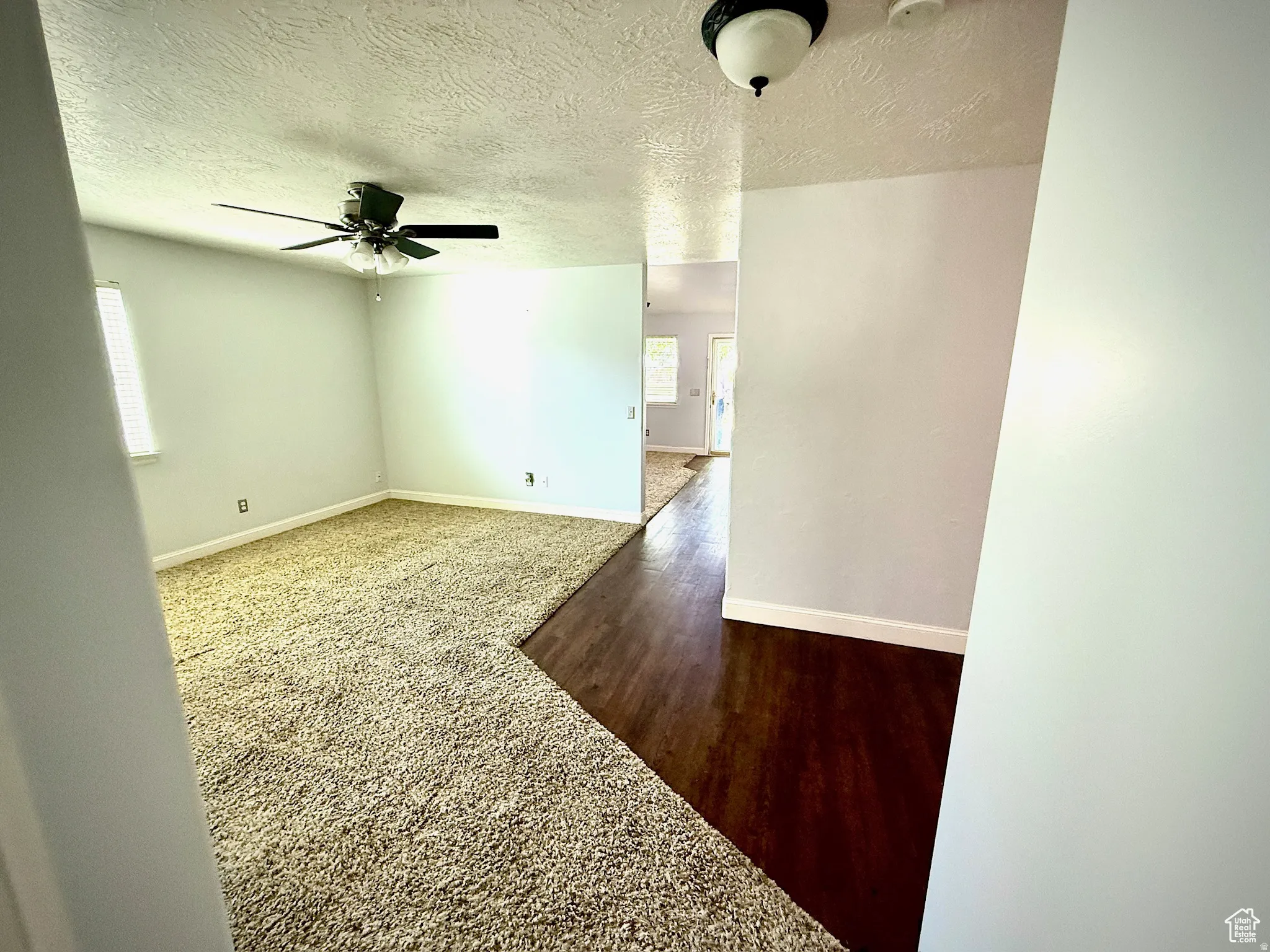 Unfurnished room with a textured ceiling, dark carpet, a ceiling fan, and dark wood finished floors