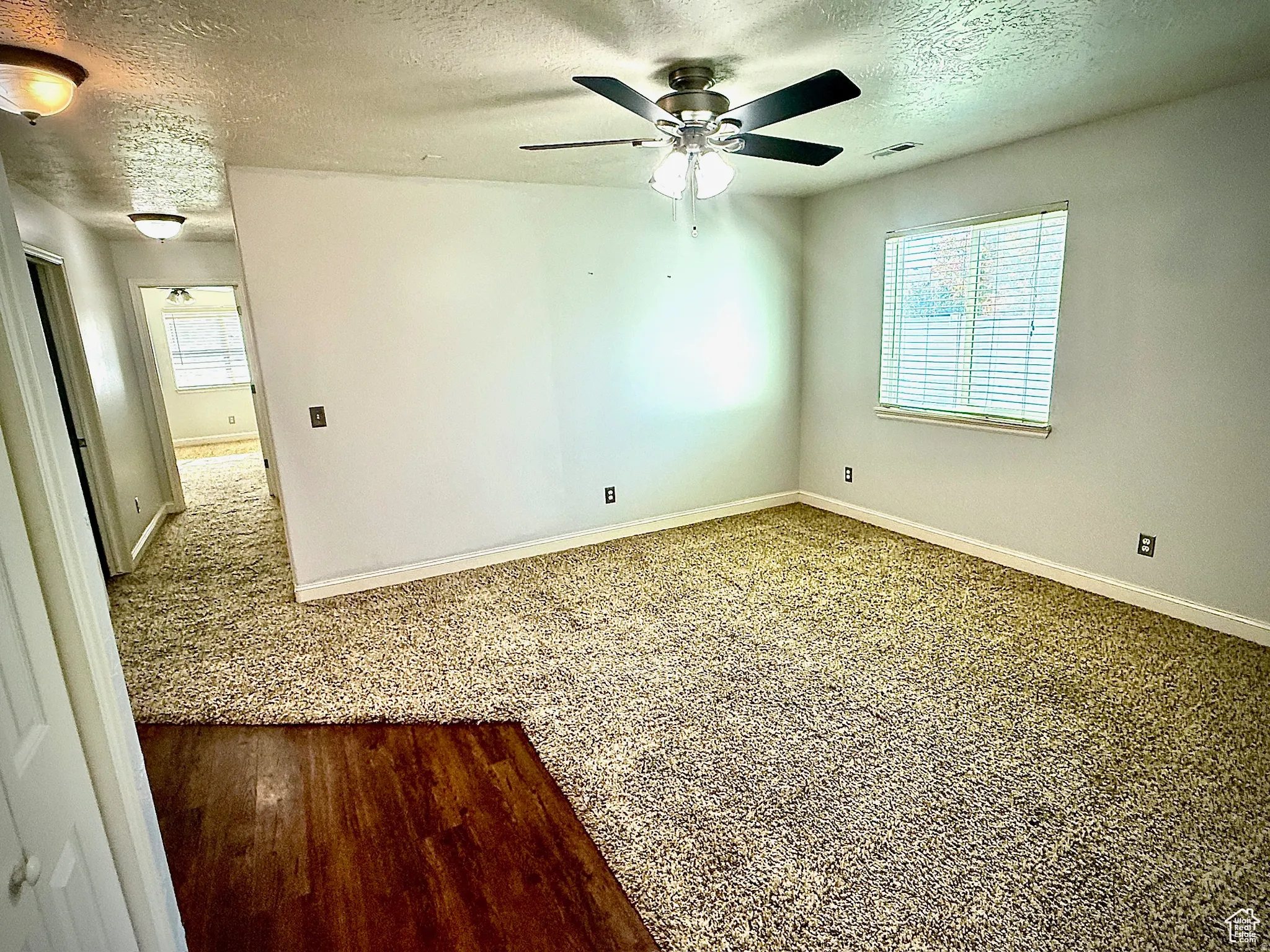 Empty room with a textured ceiling, healthy amount of natural light, ceiling fan, and carpet