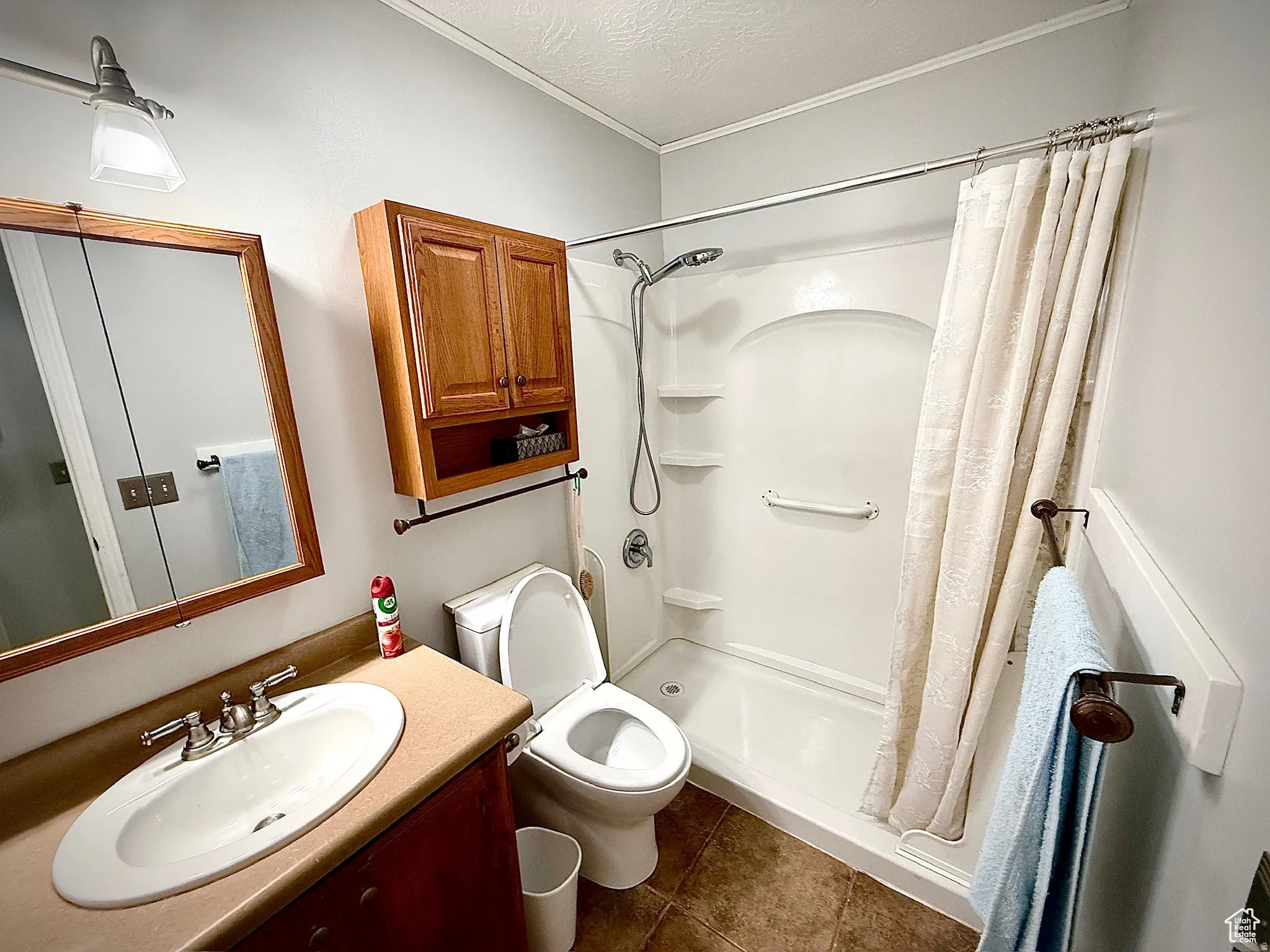 Full bath with a stall shower, vanity, a textured ceiling, dark tile patterned floors, and ornamental molding